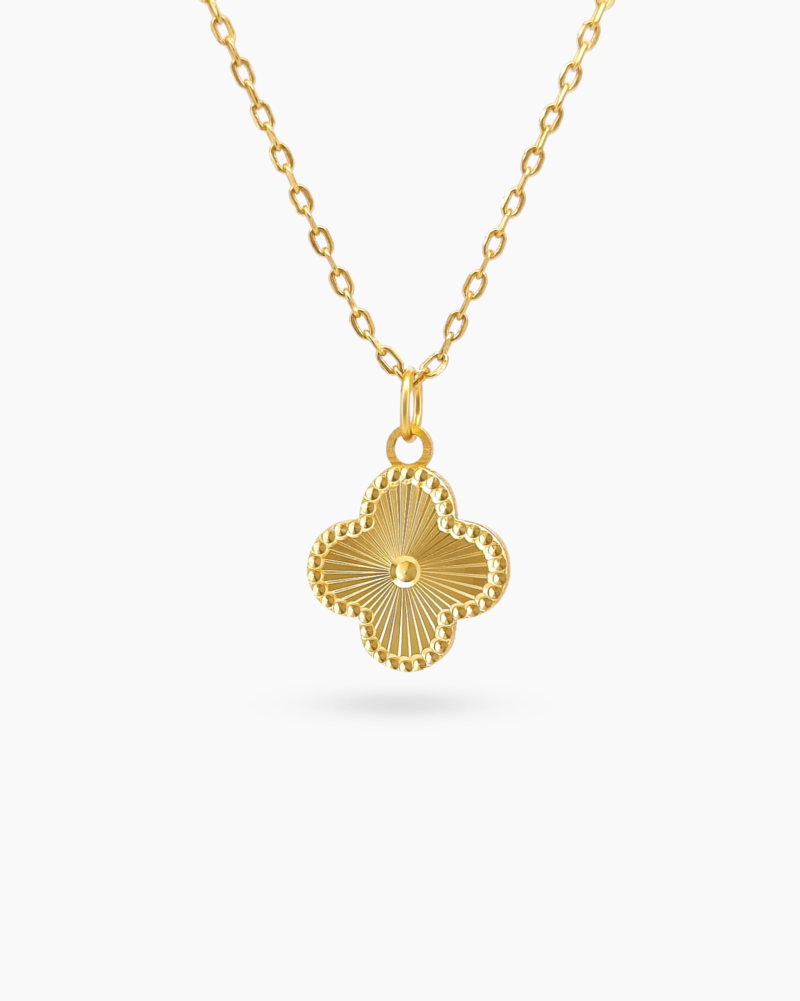 A gold-plated sterling silver necklace with a clover-shaped pendant and a sunburst-engraved surface