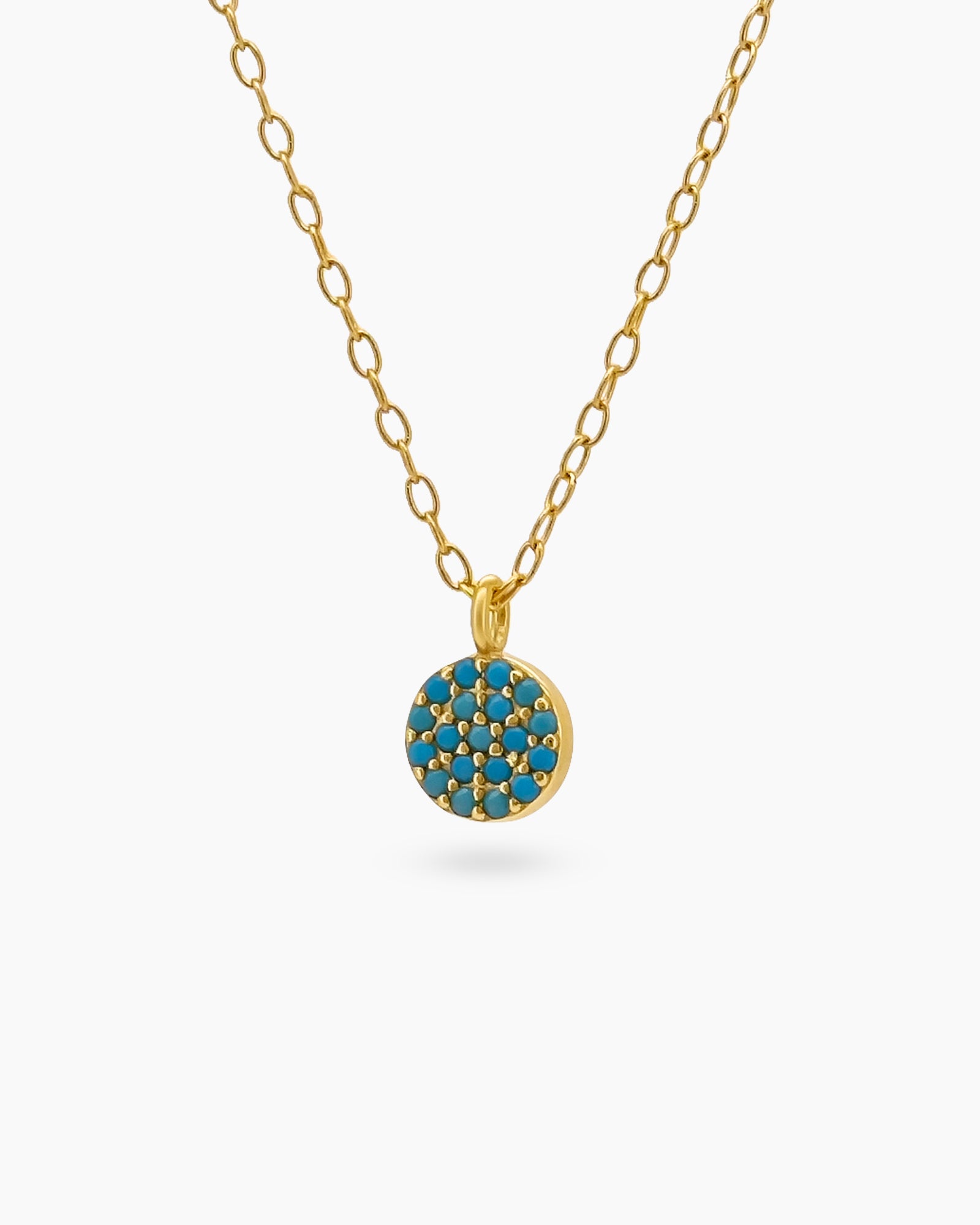 A necklace with a dainty round pendant paved with tiny turquoise zircons on a warm gold-tone setting