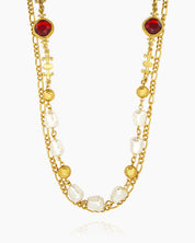 An opera-length necklace with ornate gold links, soft faux pearls, and deep red glass stones