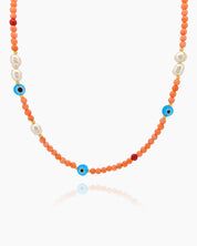 A necklace of coral-toned seed beads, freshwater pearls, and scattered evil eye charms in cobalt blue