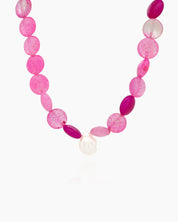 A beaded necklace with vibrant hot pink and translucent blush carnelian, accented by a single baroque pearl