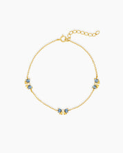 A dainty gold-toned bracelet with three tiny bows crafted from sparkling blue heart-cut zircons
