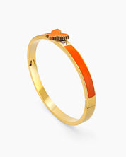 An orange hinged bangle with a sleek gold-tone design, vibrant enamel band, and a butterfly centerpiece