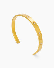 A gold bangle with a smooth, polished finish and tiny star-shaped engravings set with zircon stones