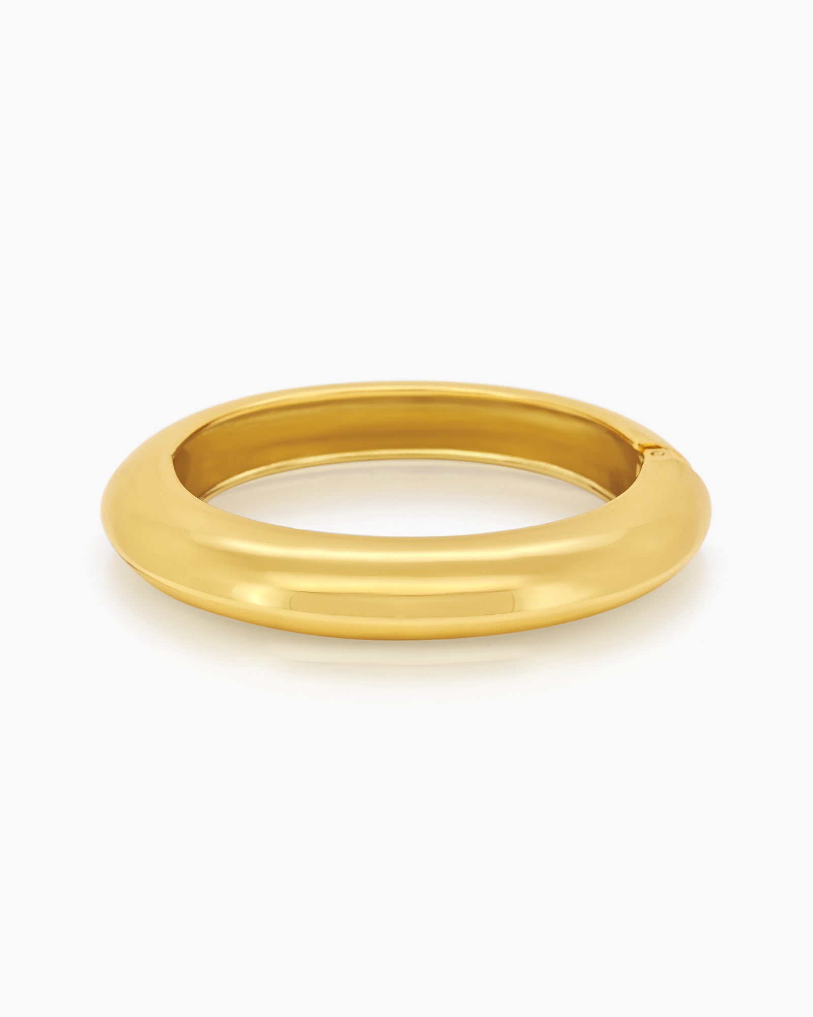 A sculptural gold bangle with a bold, rounded silhouette, high-polish finish, and seamless hinge closure