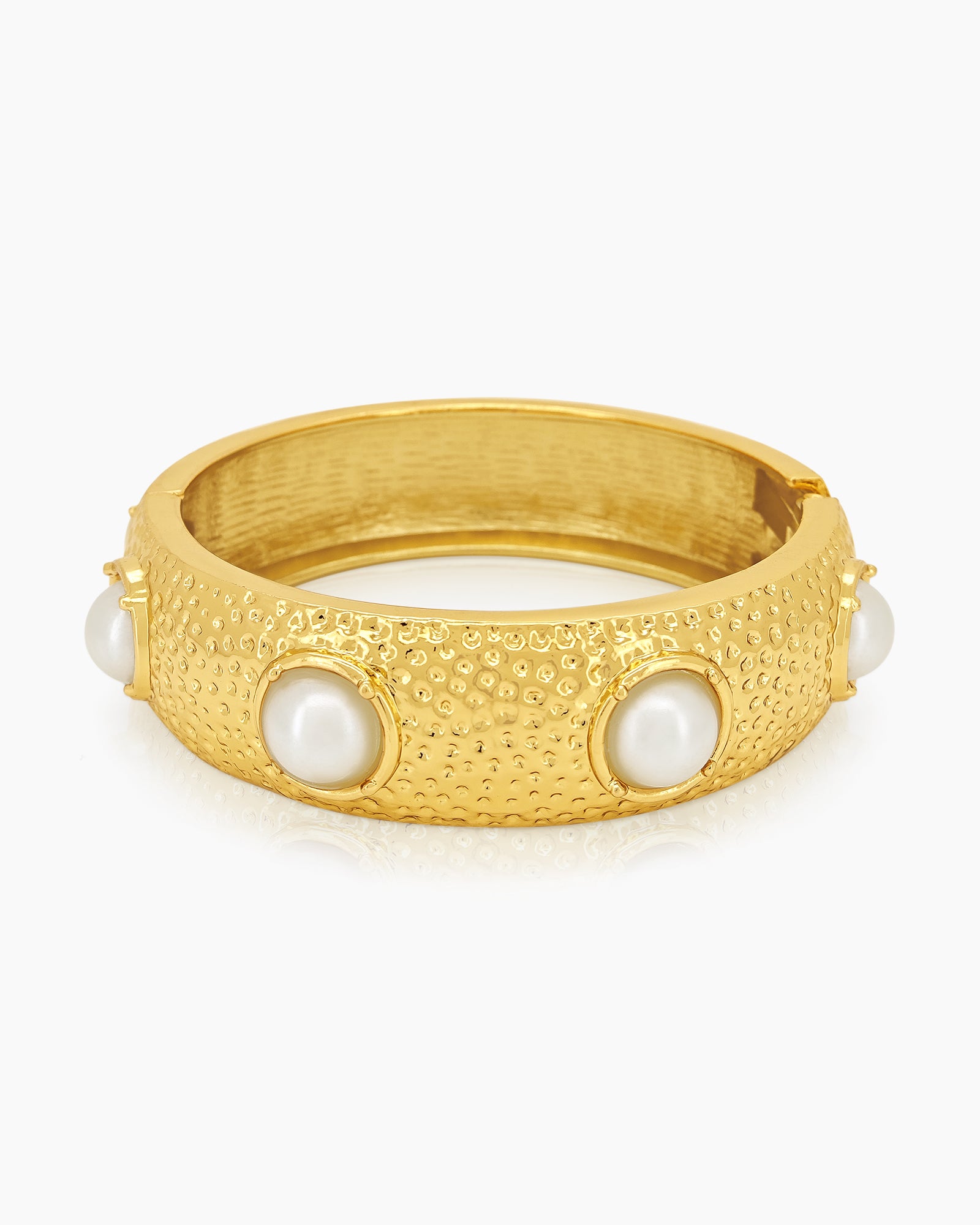 A statement bangle with a wide, hammered surface and luminous faux pearls set in raised bezels