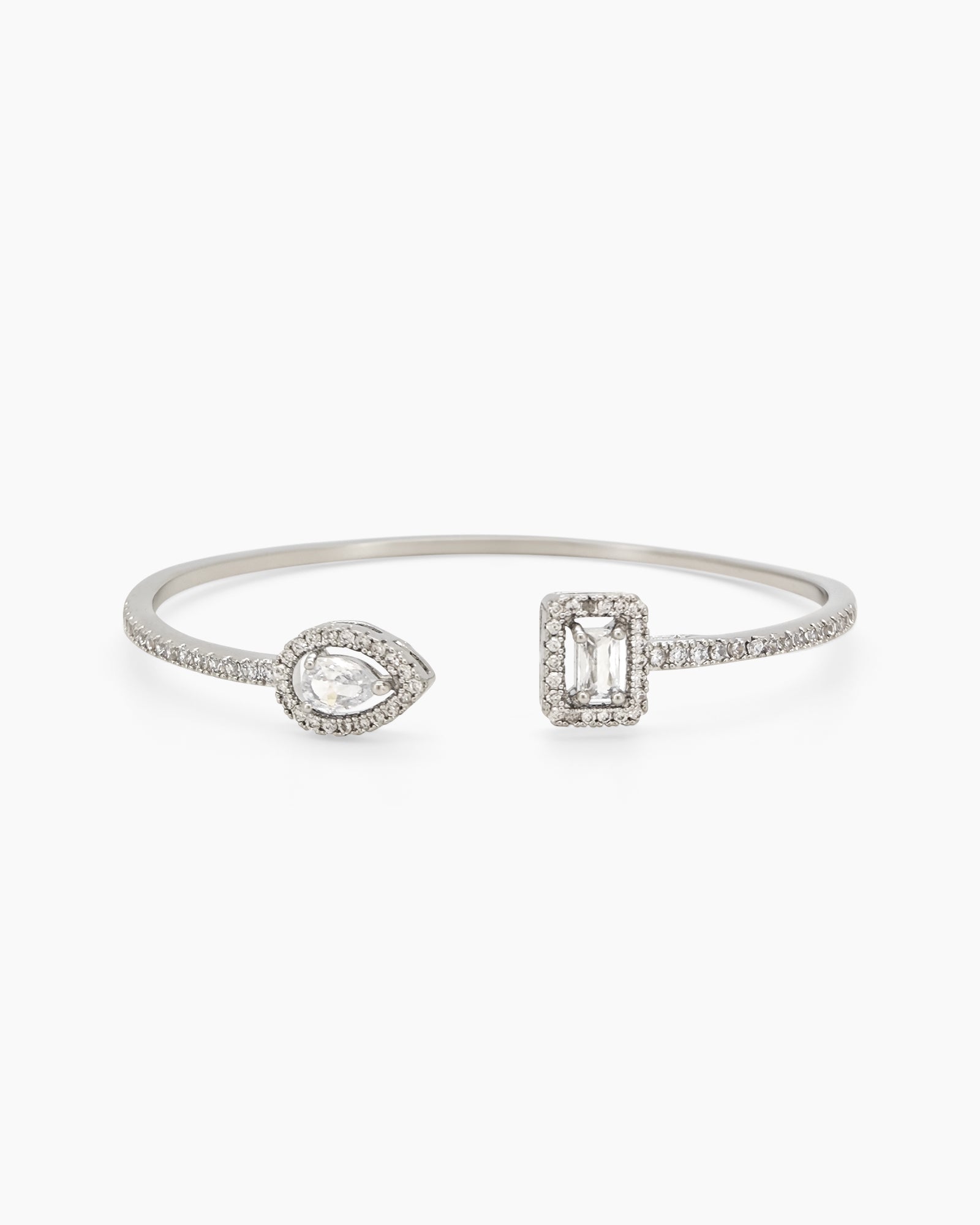 A radiant white open bangle with pear-cut and emerald-cut zircons, each framed by a halo of pavé