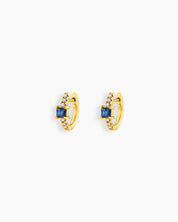 Blue huggie earrings with a sleek gold-tone hoop, a baguette-cut center stone, and a delicate arc of pavé