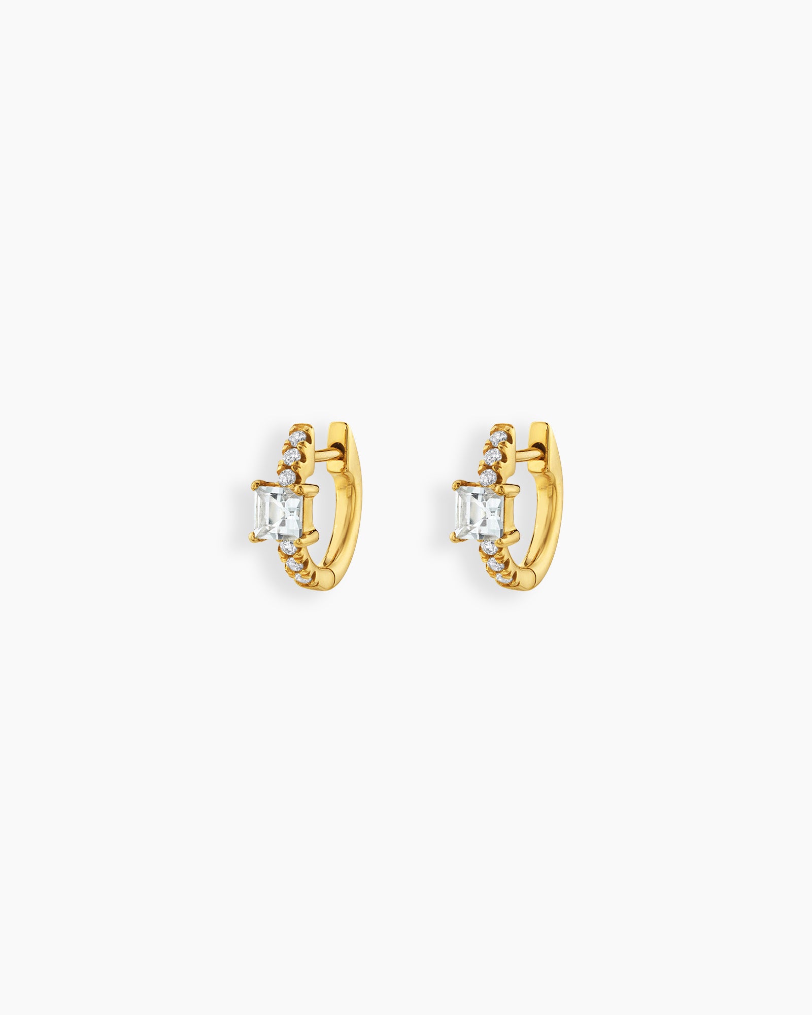 White huggie earrings with a sleek gold-tone hoop, a baguette-cut center stone, and a delicate arc of pavé