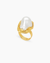 A sculptural gold ring with graceful curves and an oversized faux pearl in a textured frame
