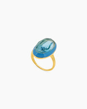 A blue-blue cocktail ring with a large, faceted oval stone framed by a glossy enamel halo on a gold band