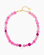 A beaded necklace with vibrant hot pink and translucent blush carnelian, accented by a single baroque pearl