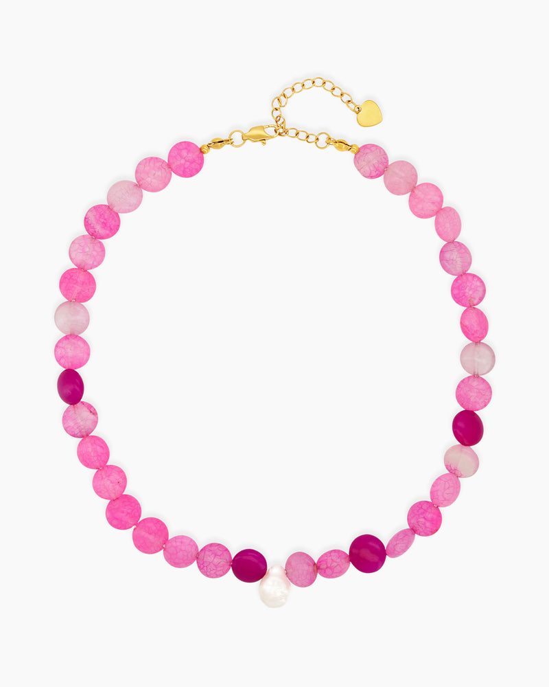 A beaded necklace with vibrant hot pink and translucent blush carnelian, accented by a single baroque pearl