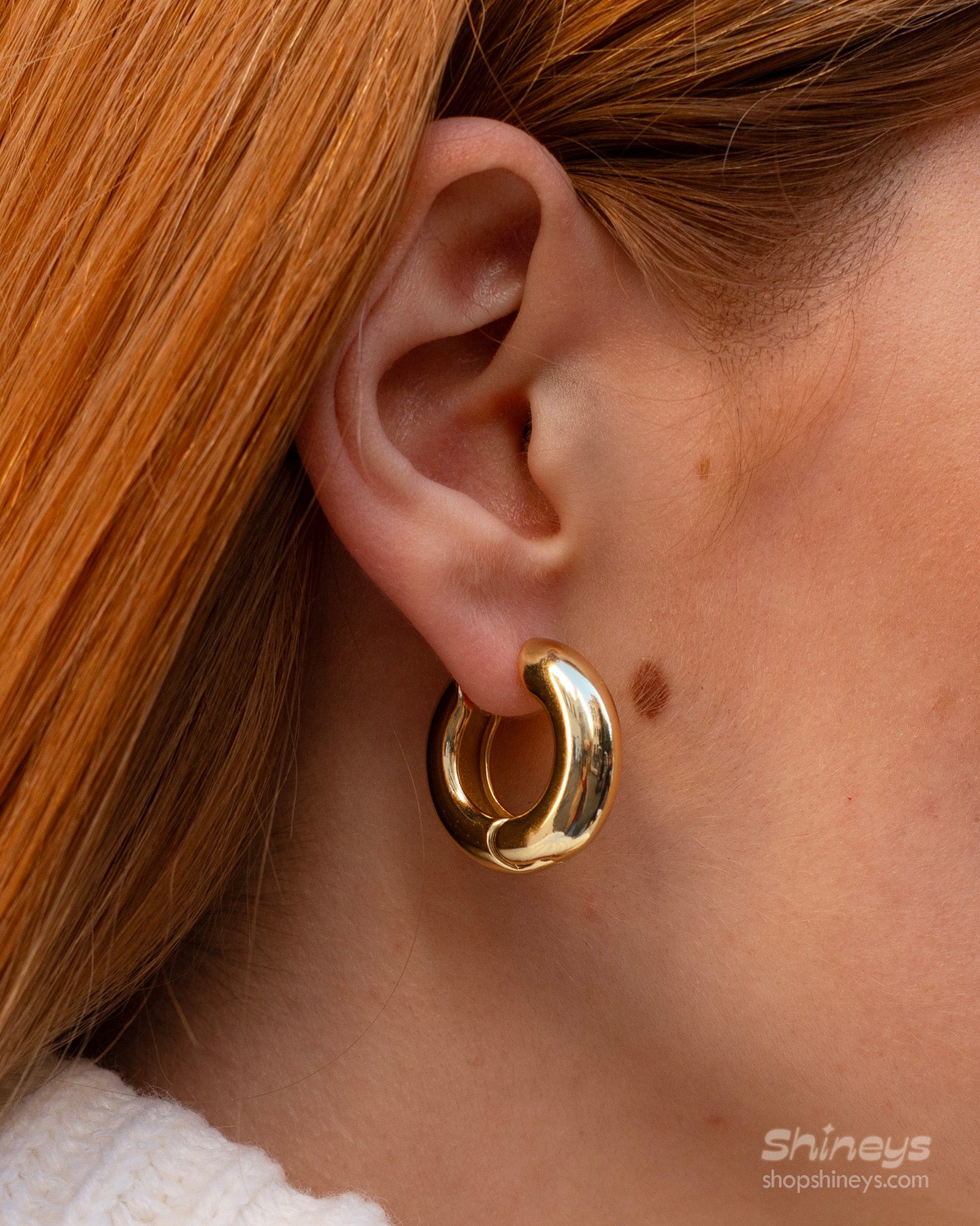 Chunky gold hoop earrings sculpted into a perfect round with a smooth surface that catches the light