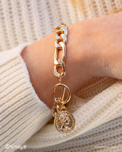 A gold bracelet with chunky chain links, a toggle clasp, and a medallion-style coin charm