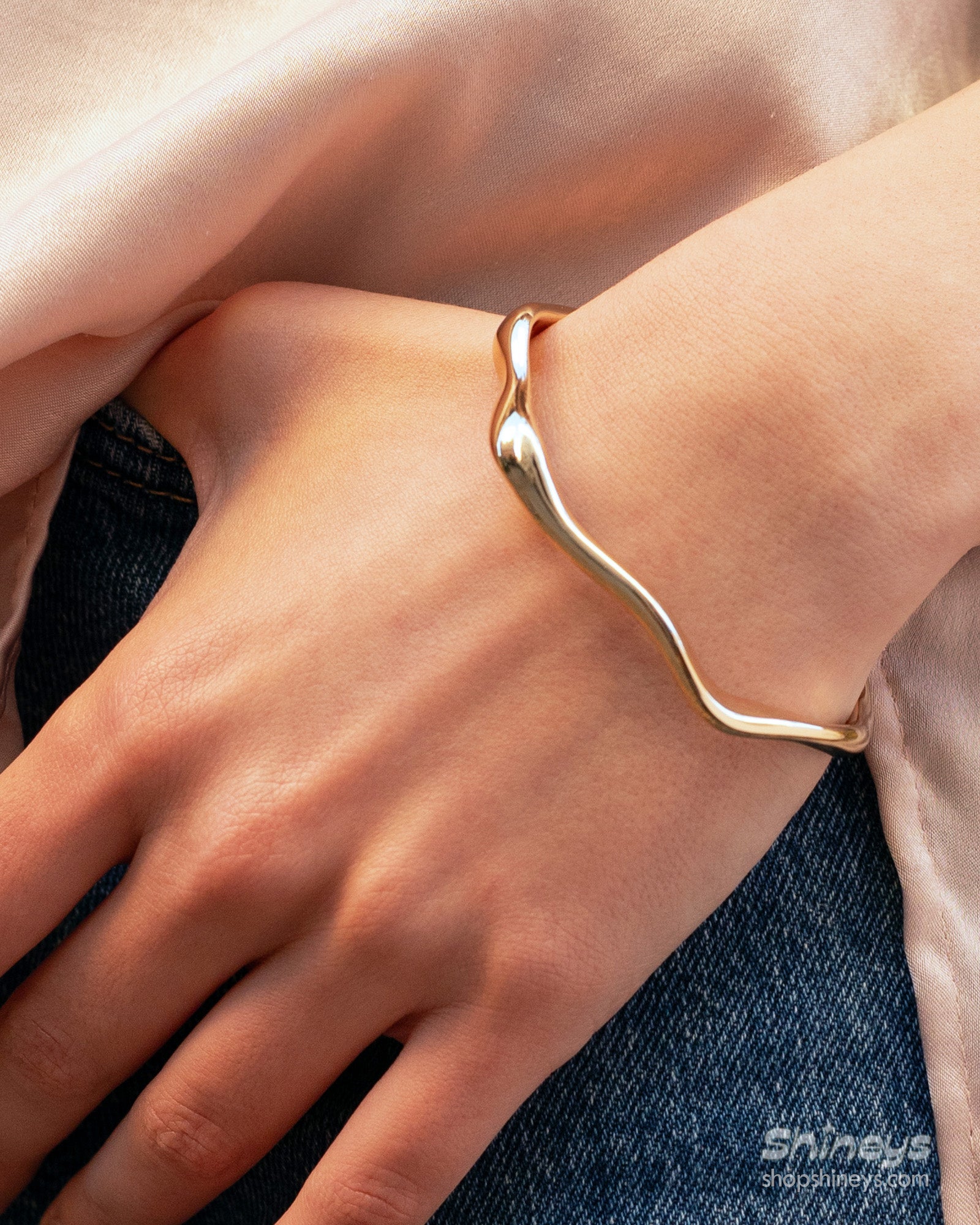 A silver open bangle with soft, wavy curves that wrap gently around the wrist for a refined look