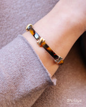 A double-wrapped bangle in high-gloss acrylic with a tortoiseshell effect and polished cross details