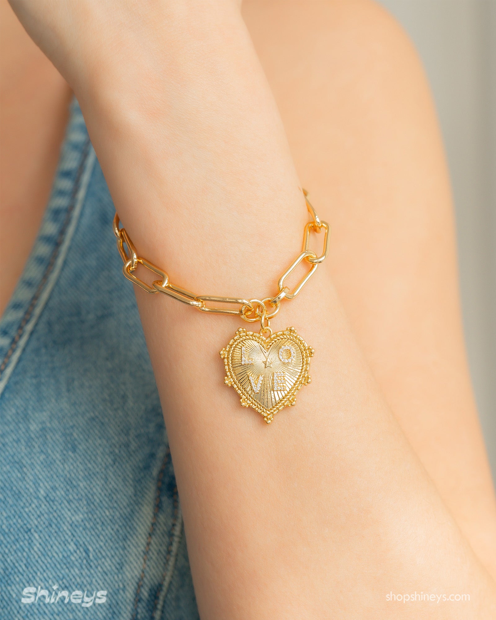 A paperclip chain bracelet with a radiant, textured heart pendant engraved with the word "love"