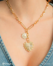A necklace with a sunburst charm and a radiant, heart-shaped pendant on an elongated gold link chain