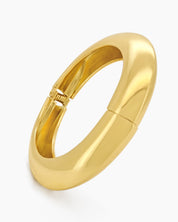 A sculptural gold bangle with a bold, rounded silhouette, high-polish finish, and seamless hinge closure