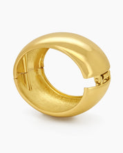 A gold bangle with a wide, mirror-like surface and a curved silhouette for a sleek, modern look