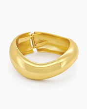 A gold hinged bangle with smooth curves and a fluid, wave-like silhouette for a minimalist focus