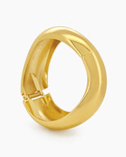 A gold hinged bangle with smooth curves and a fluid, wave-like silhouette for a minimalist focus