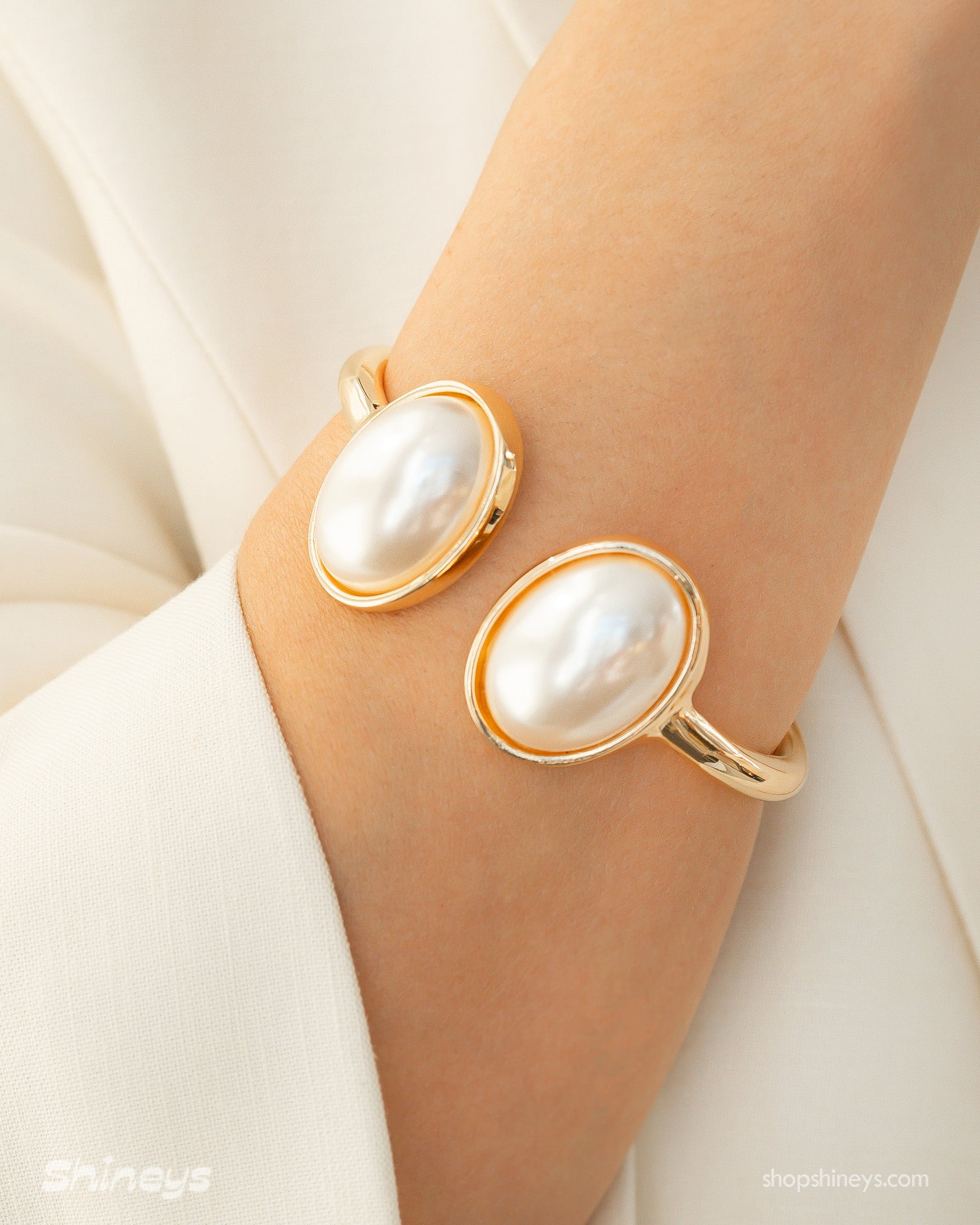 A polished gold cuff with two oversized faux pearls in a glossy frame and a secure hinge closure