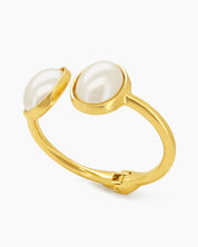 A polished gold cuff with two oversized faux pearls in a glossy frame and a secure hinge closure