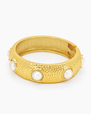 A statement bangle with a wide, hammered surface and luminous faux pearls set in raised bezels
