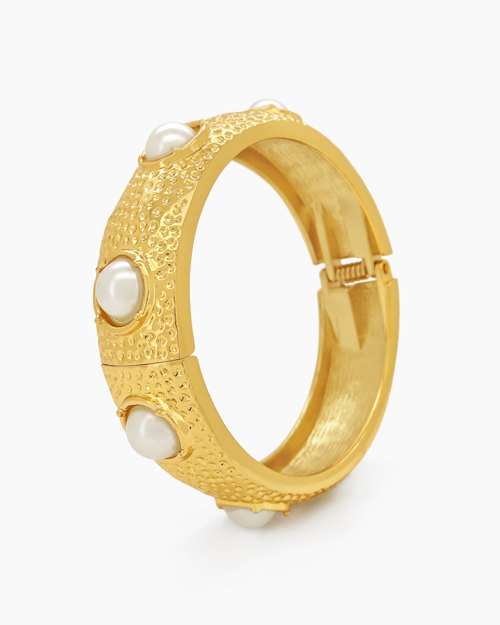 A statement bangle with a wide, hammered surface and luminous faux pearls set in raised bezels