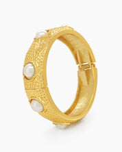 A statement bangle with a wide, hammered surface and luminous faux pearls set in raised bezels
