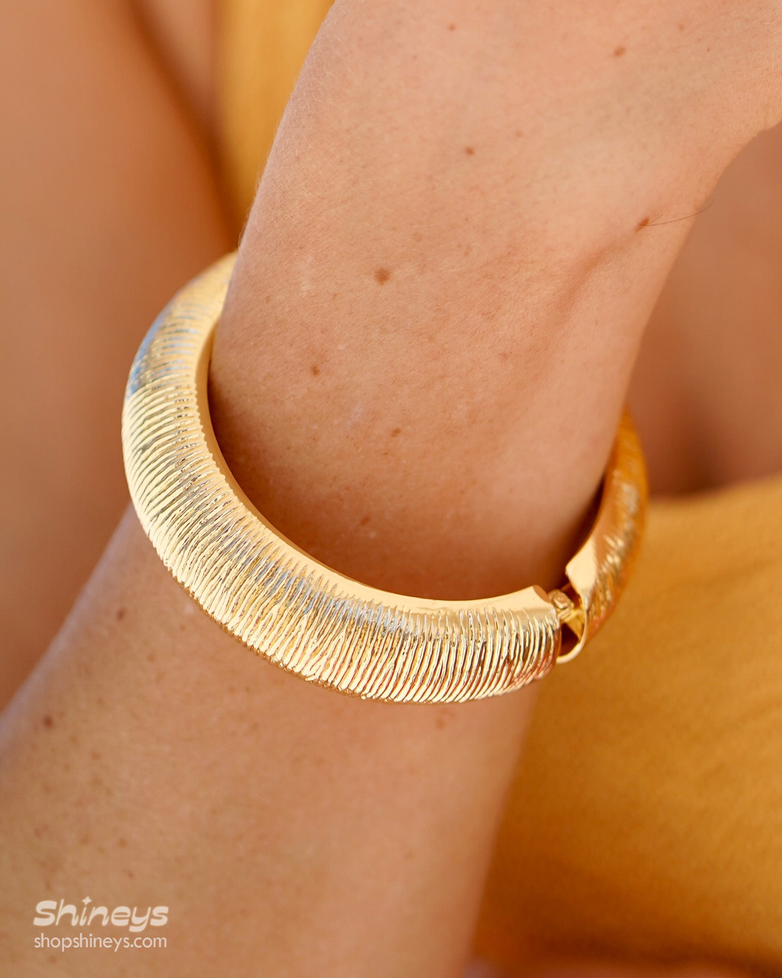 A classic gold bangle with a deeply etched texture, high-shine finish, and a secure hinge clasp