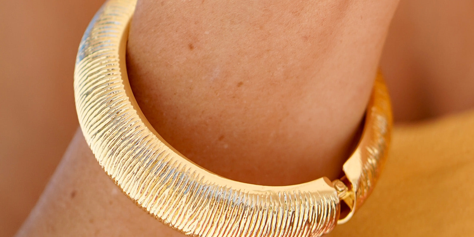 A classic gold bangle with a deeply etched texture, high-shine finish, and a secure hinge clasp