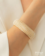 A gold-tone bangle encrusted with rows of tiny faux pearls, creating a soft, sculptural rhythm