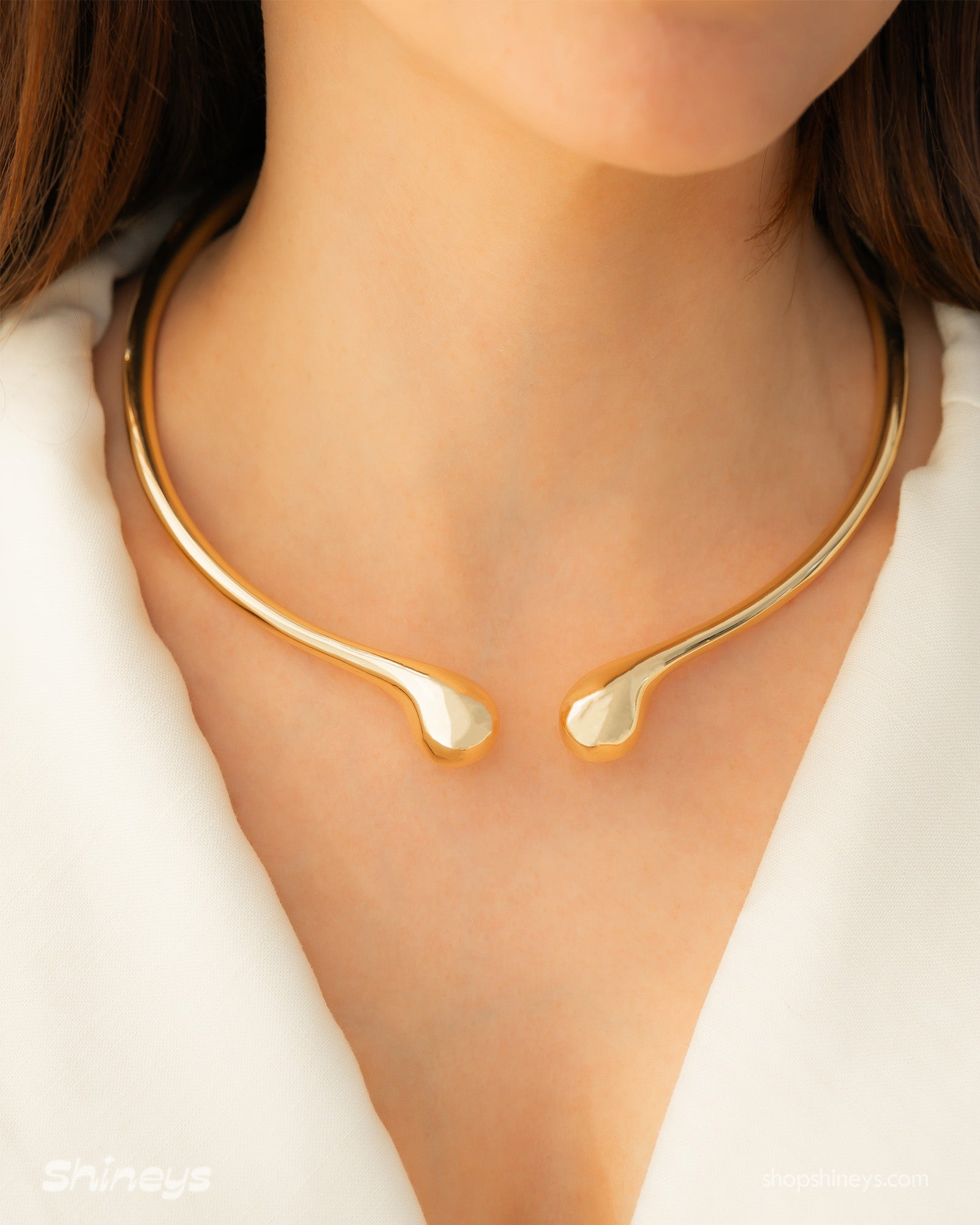 A polished gold necklace featuring a clean, narrow torque design with smooth, droplet-like tips