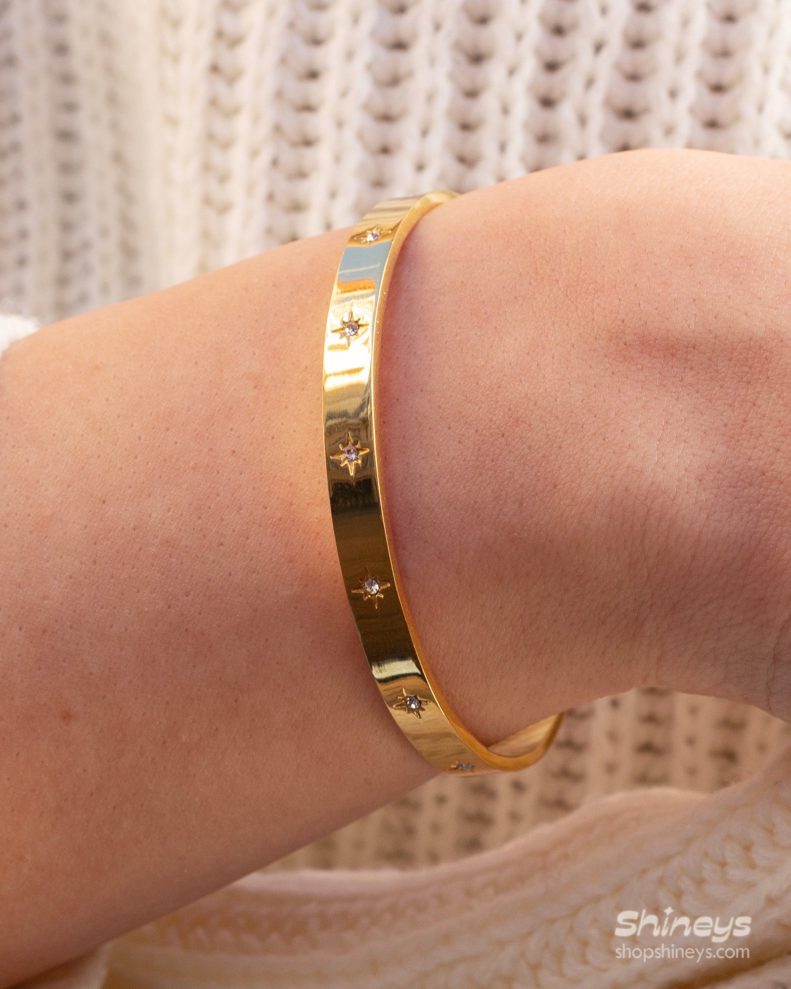 A gold bangle with a smooth, polished finish and tiny star-shaped engravings set with zircon stones
