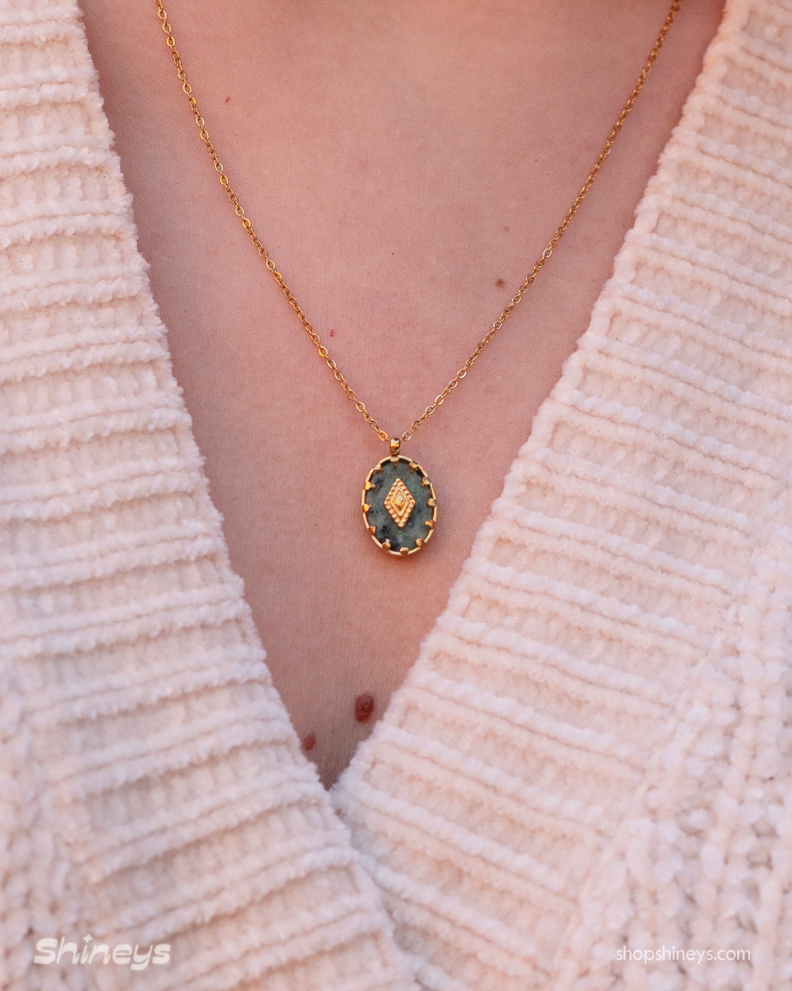 A necklace with a green african pine stone pendant in a textured gold-toned bezel with a diamond motif