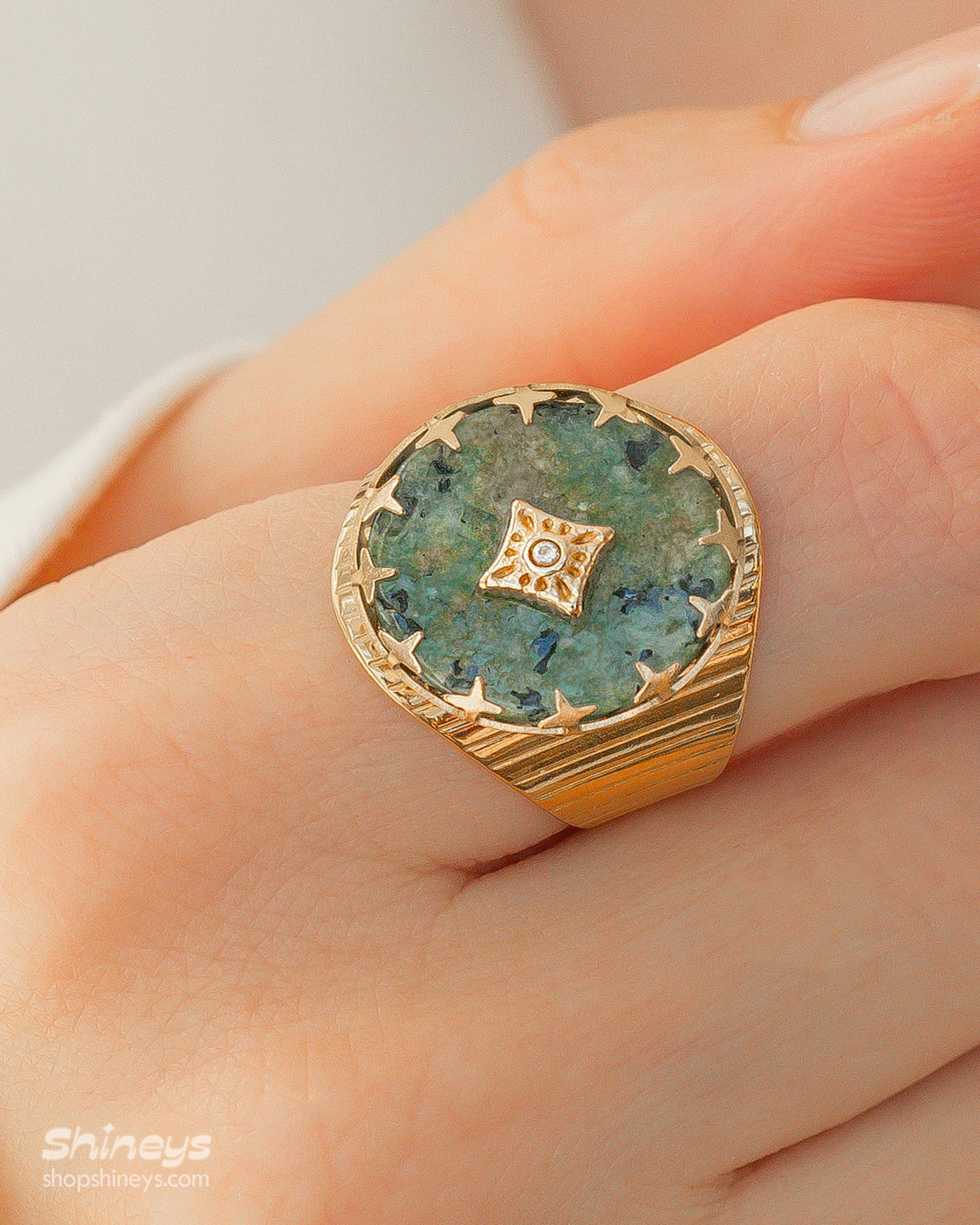 An adjustable ring with a textured gold band and a green african pine center stone, crowned by a crystal