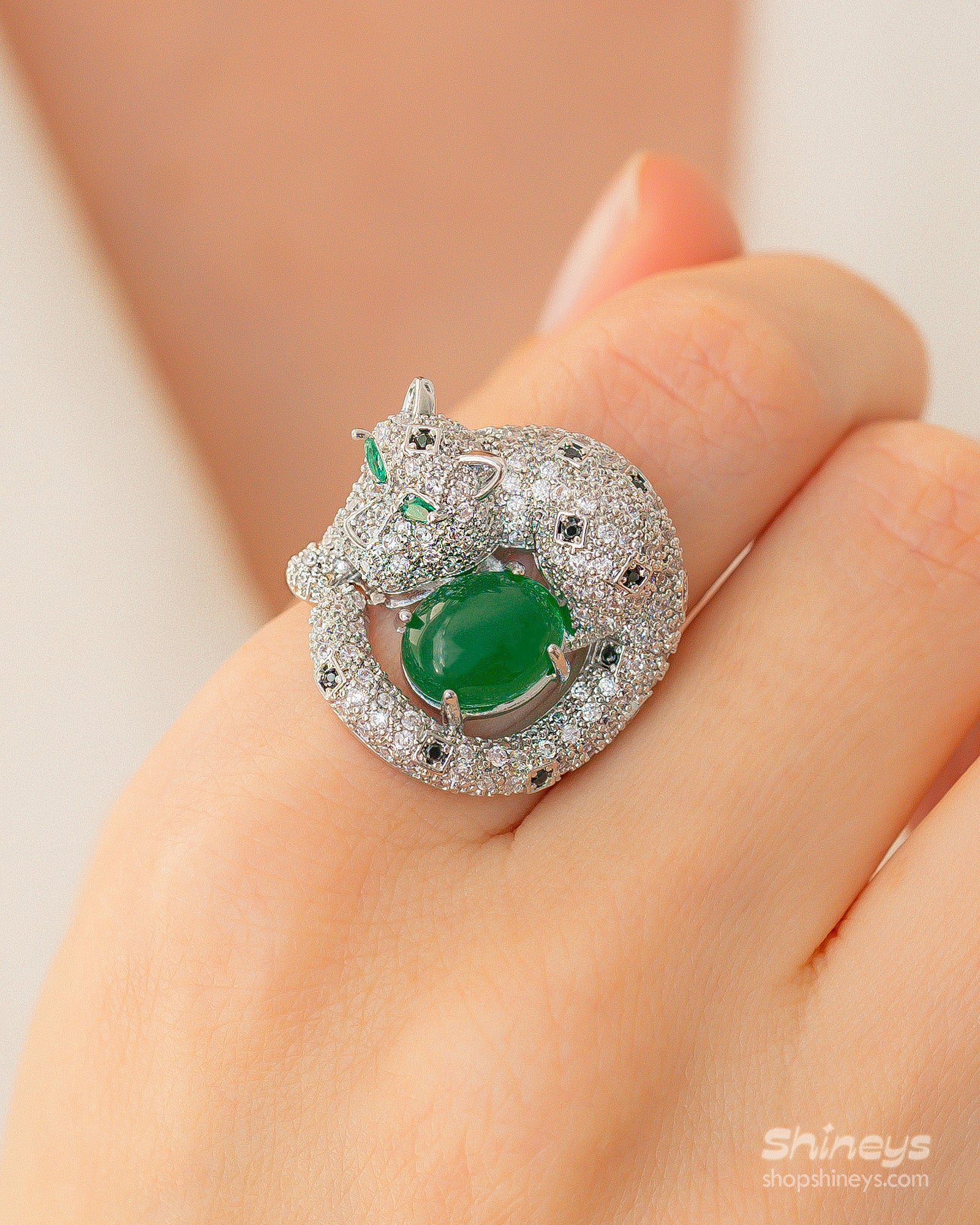 An adjustable silver-tone ring with a zircon-encrusted panther curled around a rich green jade stone