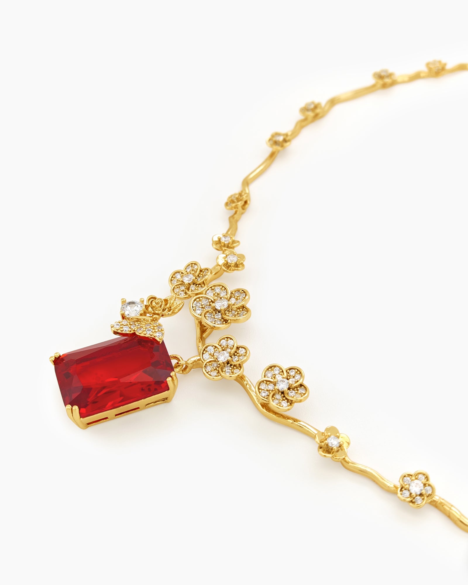 A jewelry set with gold-toned floral links, fine zircons, and a striking, deep crimson emerald-cut stone