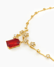 A jewelry set with gold-toned floral links, fine zircons, and a striking, deep crimson emerald-cut stone