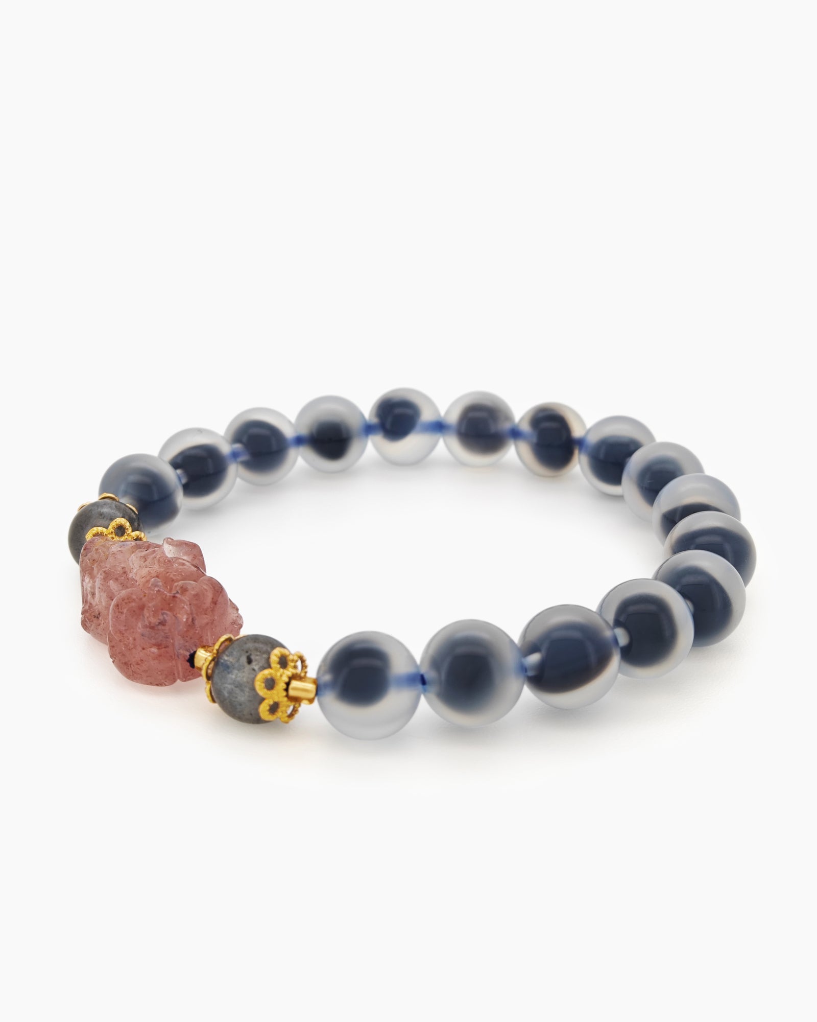 A bracelet of smooth blue agate stones with a central carved pink charm and golden accents