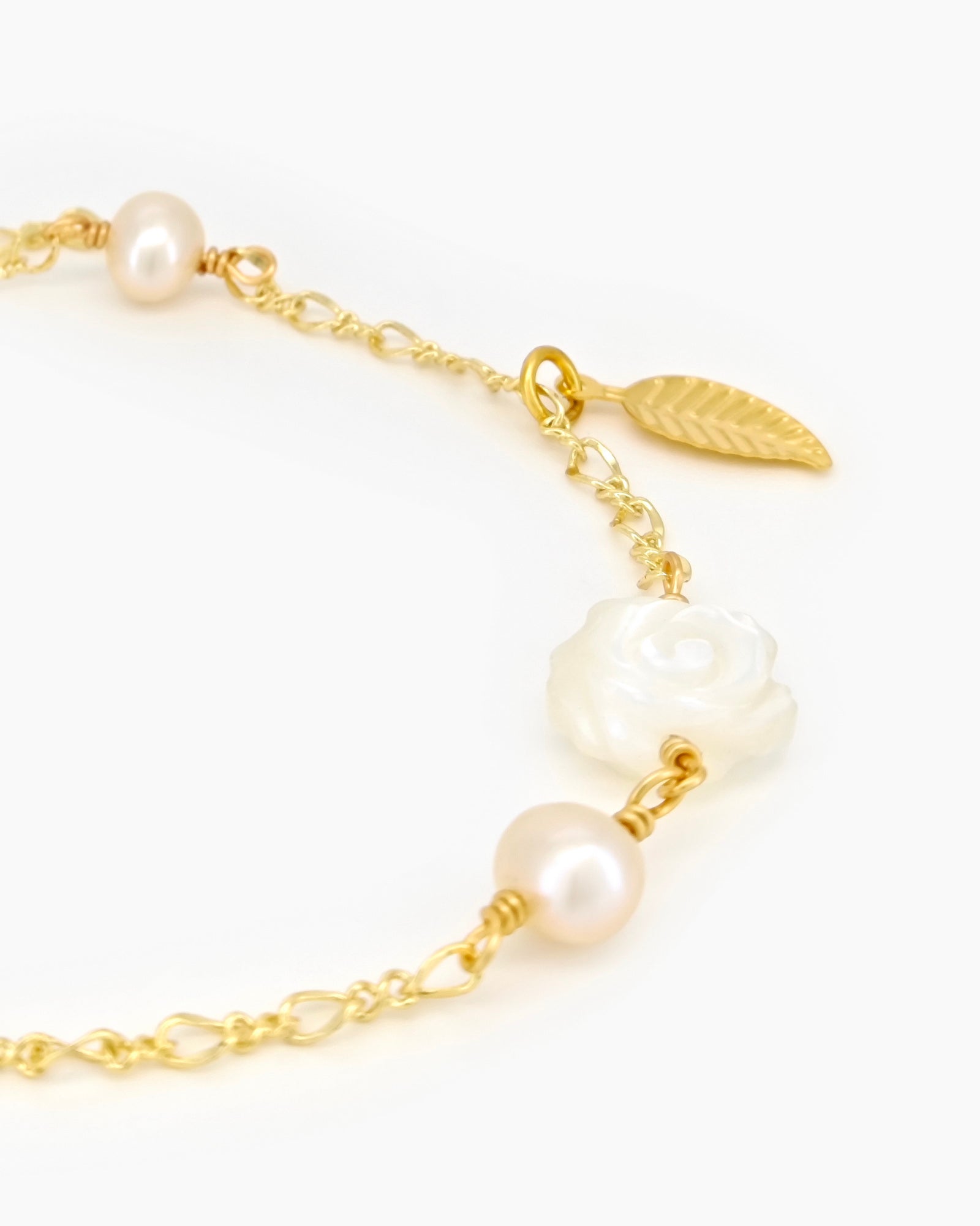 A bracelet with a finely sculpted white rose centerpiece, framed by freshwater pearls and a golden leaf accent
