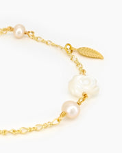 A bracelet with a finely sculpted white rose centerpiece, framed by freshwater pearls and a golden leaf accent