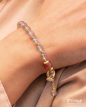 A bracelet of hand-strung natural moonstone beads with a single strawberry quartz bead and golden accents