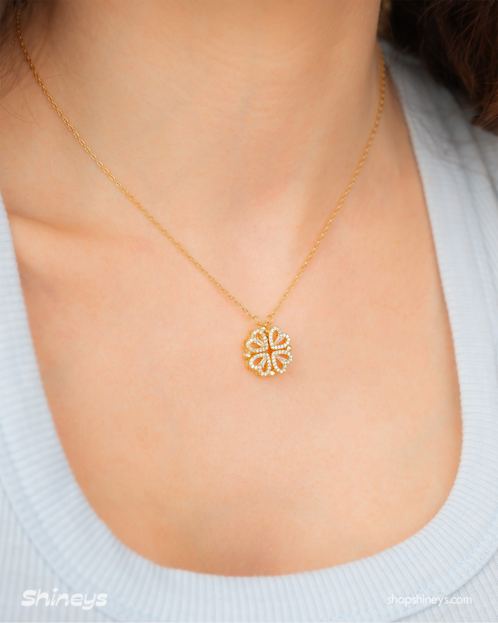 A gold necklace with a clover-inspired pendant of four pavé-outlined hearts that opens up