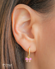 Playful gold hoop earrings with a cascade of cubic zirconia stones and a dangling soft pink enamel bow