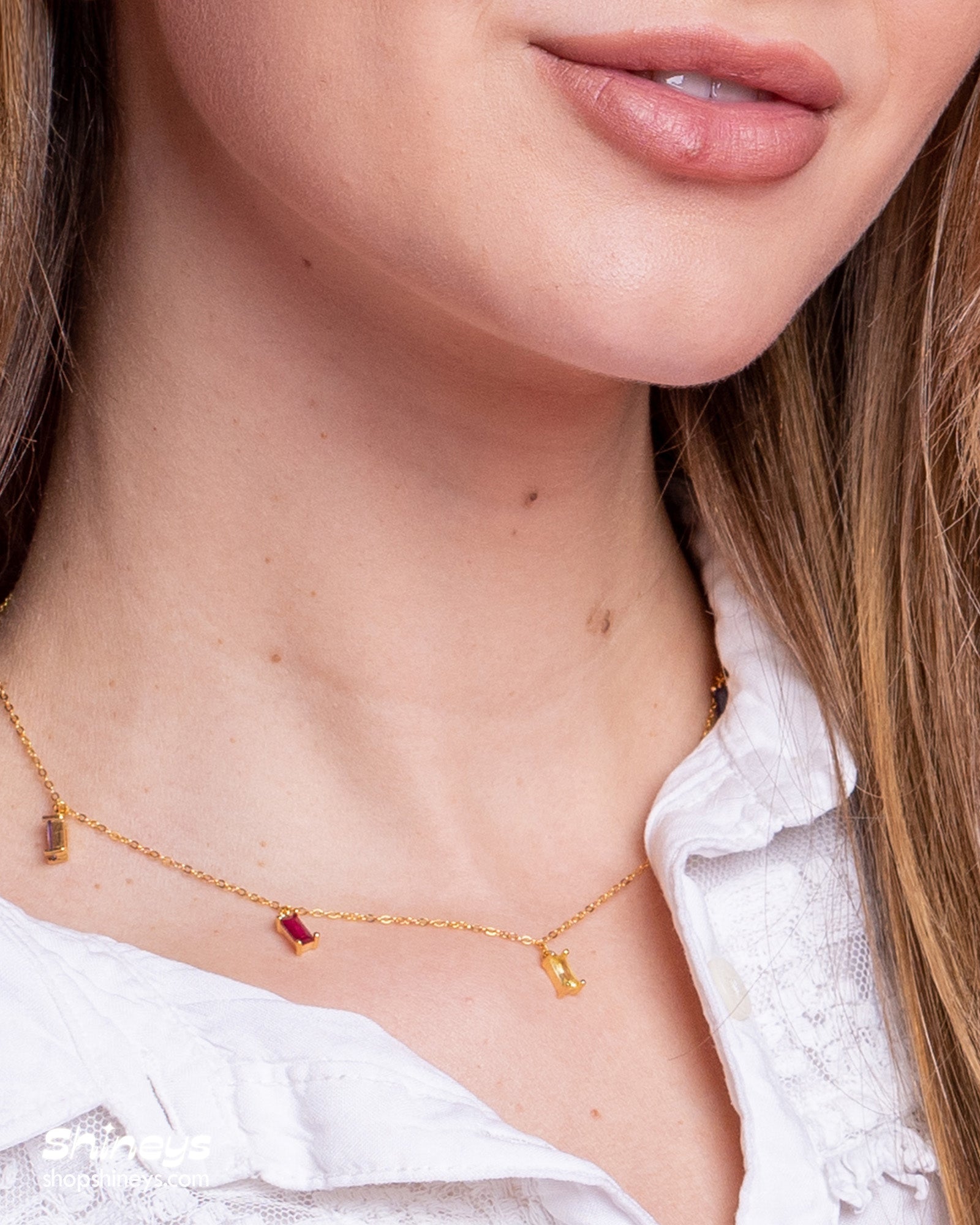 A gold necklace with a delicate chain adorned with dainty baguette-cut zircon charms in a rainbow of hues