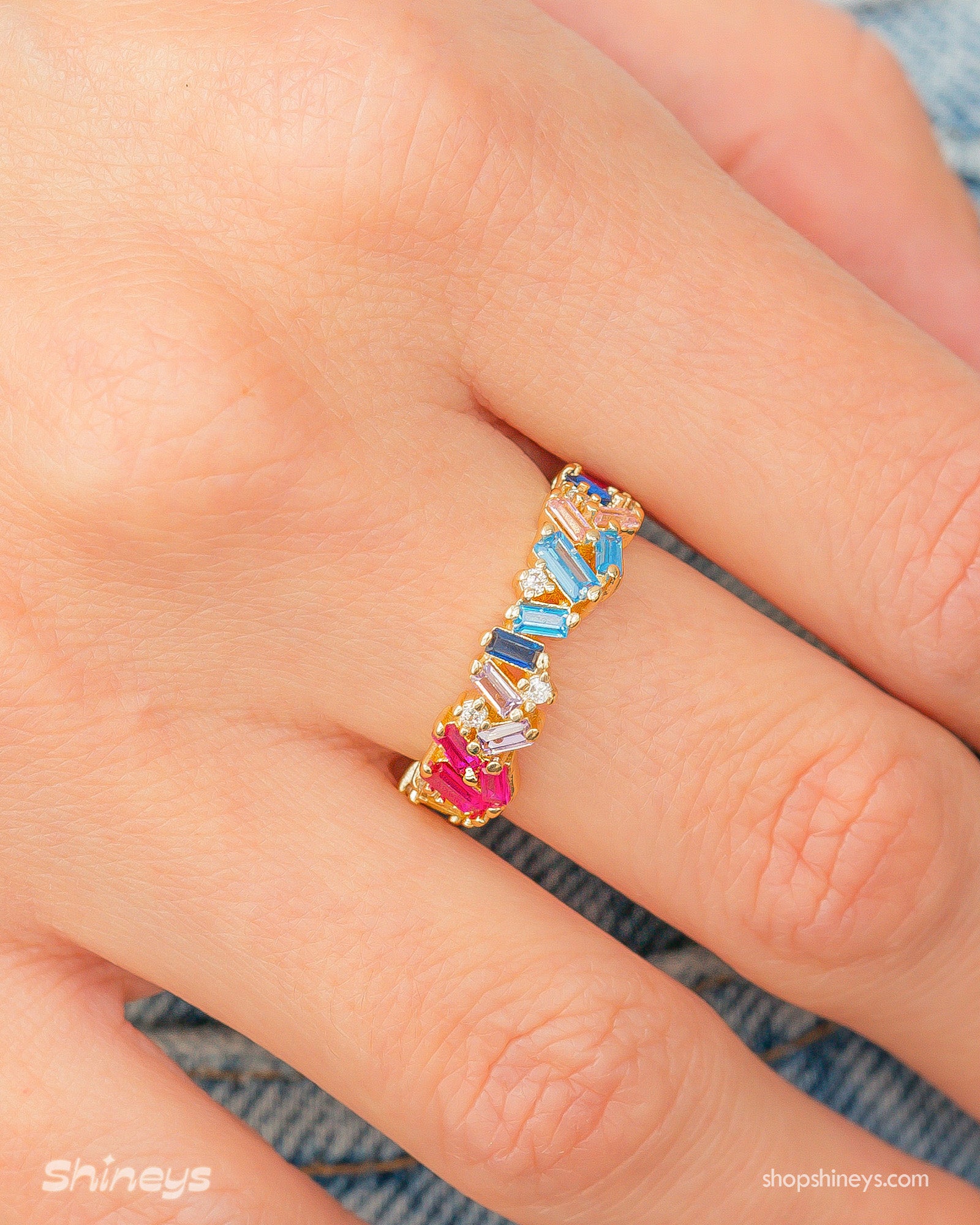 A band ring with baguette-cut zircons in dreamy shades, set at a playful, tilted angle on a gold band